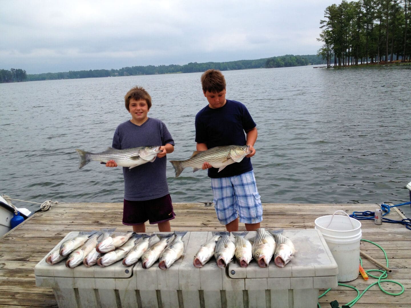 Kids showing fresh-caught fish beside lake